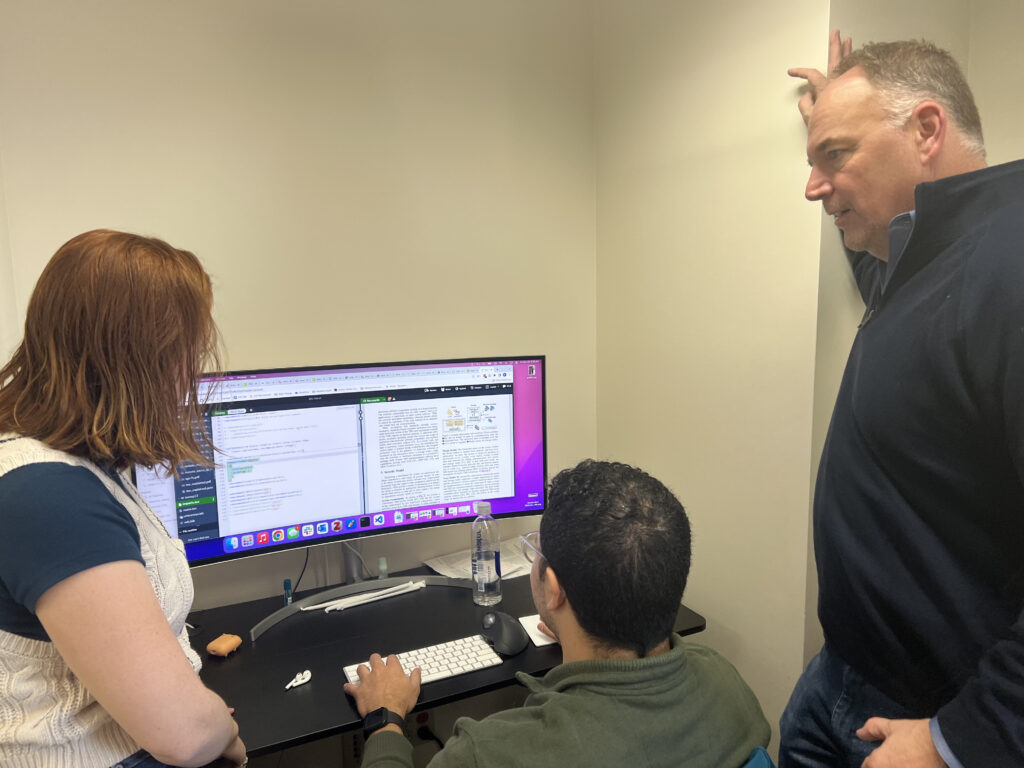 Rachel King, Quinn Burge and Patrick McDaniel gather around a computer to discuss a project.