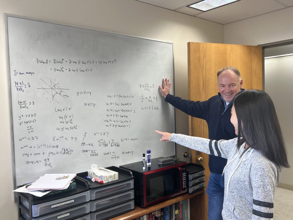 Patrick McDaniel and Kunyang Li discuss calculations that are on a whiteboard