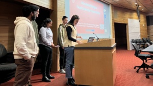 Six students present in front of a group with a slide presentation in the background