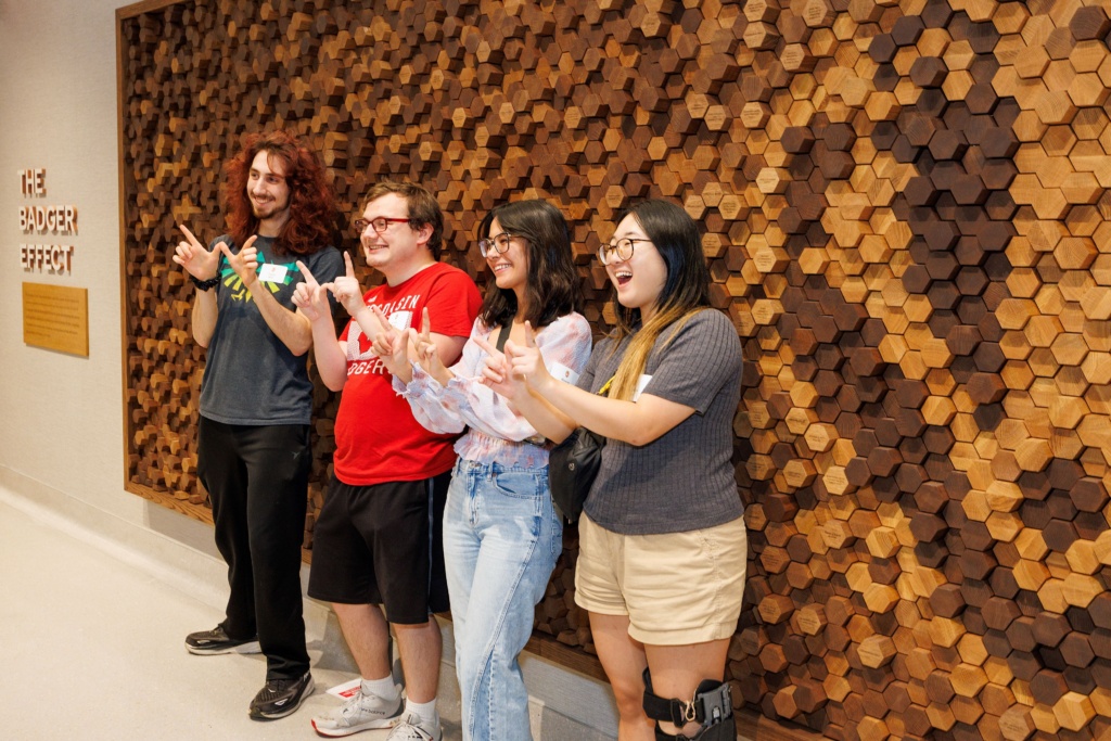 Students stand in front of Badger Effect Wall and pose
