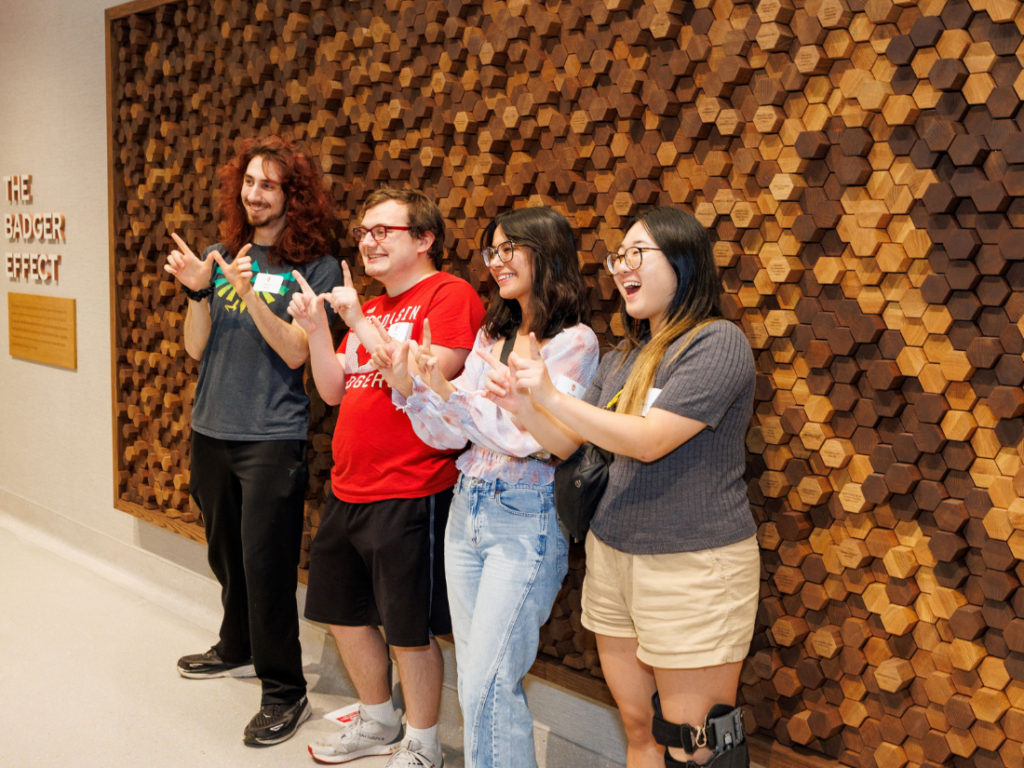 Students stand in front of Badger Effect Wall and pose