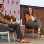 Professor of Computer Science Suman Banerjee and Epic founder Judy Faulkner seated on stage in modern chairs during a discussion, with University of Wisconsin logos on the backdrop behind them.