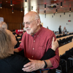 Award winner Prudence Dalrymple embraces an event attendee in a modern room.
