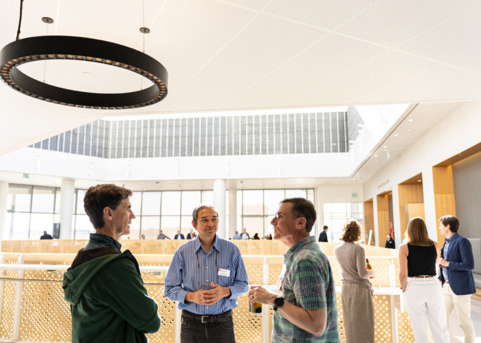 Faculty, staff, and guests gather in a light-filled, modern atrium.