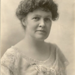 Vintage sepia portrait of a woman in an elegant lace dress with intricate floral patterns and a decorative brooch.